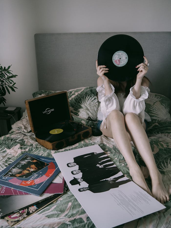 about-04 Woman holding a vinyl record on a bed with a record player and album covers, creating a cozy bedroom vibe.
