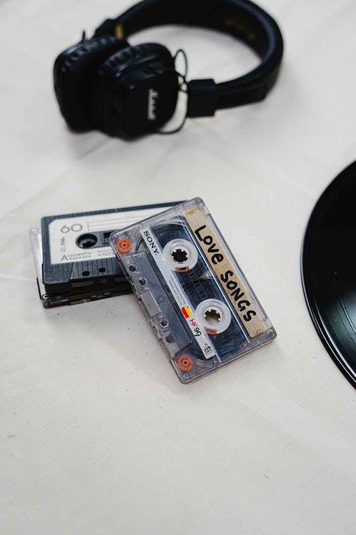 about-002 Flat lay of nostalgic cassette tapes labeled 'Love Songs' with black headphones and vinyl record.